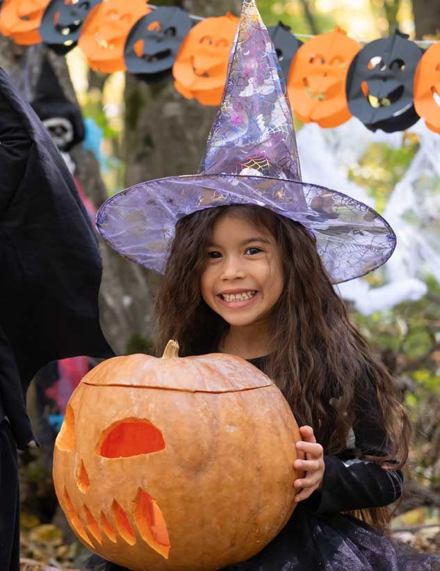 Cute girl in a witch costume sitting at a campsite, holding a pumkin